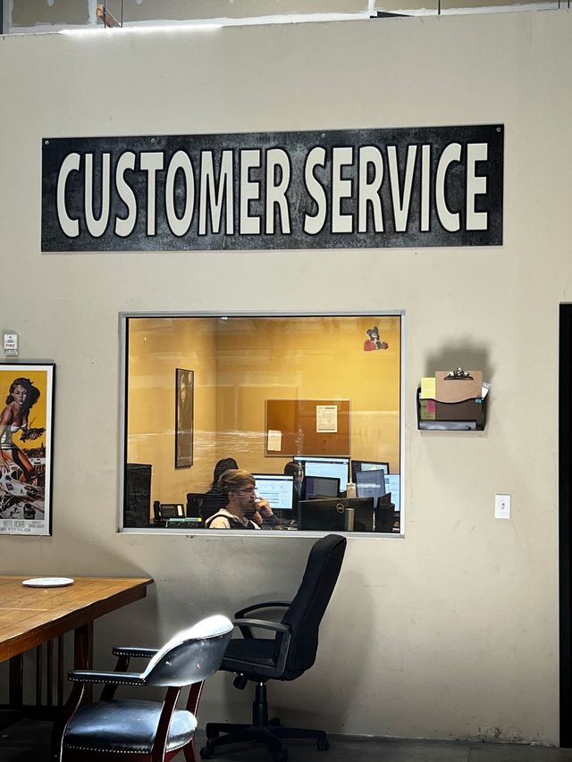 Customer service office window under a large Customer Service sign, with staff working at their computers inside