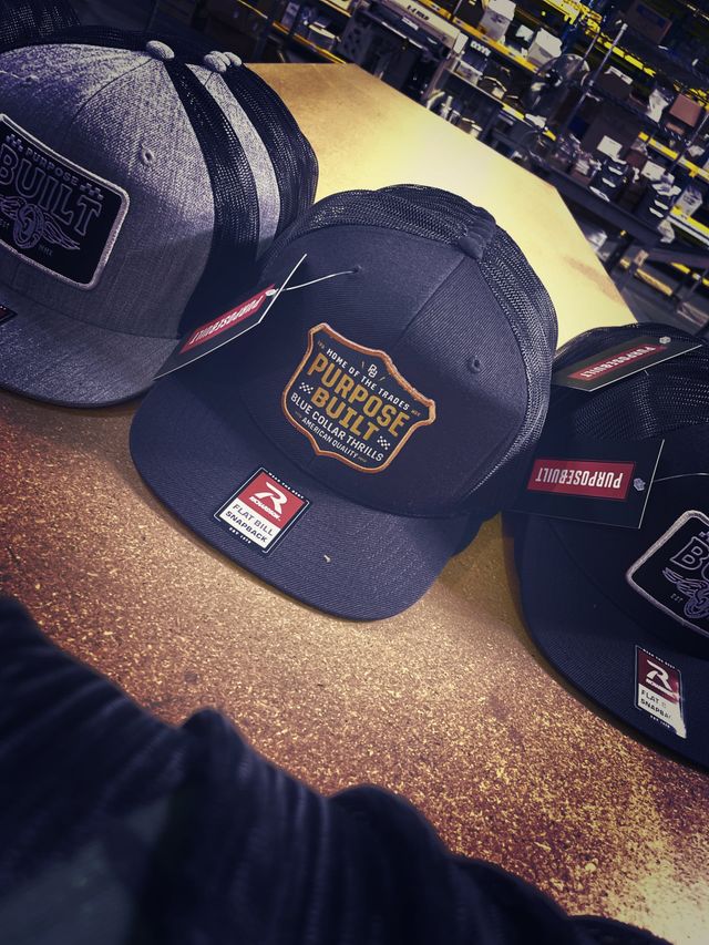Navy snapback caps with an embroidered Purpose Built patch on a work table