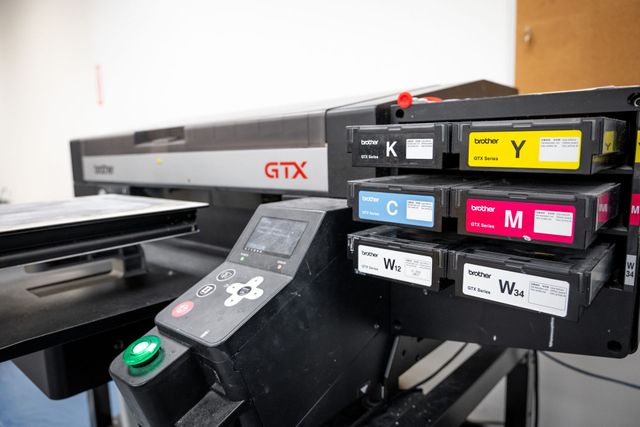 Brother GTX printer control panel beside its black, cyan, magenta, yellow and white ink cartridges