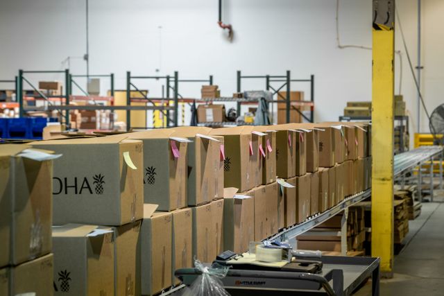 Rows of packed cardboard shipping boxes on the fulfillment floor, with a roller conveyor and warehouse racks behind