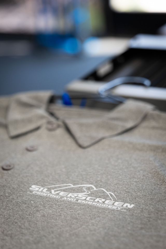 Close-up of a gray polo shirt with a white Silverscreen Printing and Embroidery logo transfer on the chest