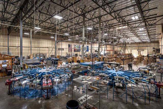 Silverscreen's screen printing floor in Reno, with rows of blue automatic carousel presses under a high warehouse ceiling